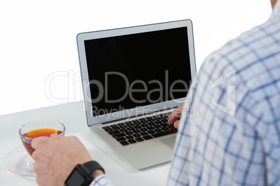 Male executive using laptop while having lemon tea