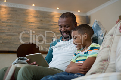 Father and son using digital tablet on sofa in living room