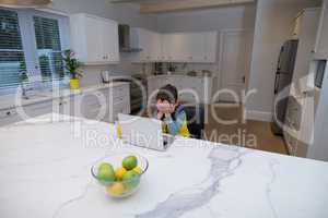 Upset boy using laptop in kitchen