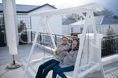 Couple having coffee on a porch swing in balcony