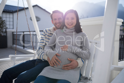Man and pregnant woman touching her belly in balcony