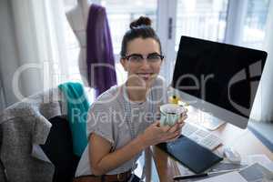 Smiling female designer having coffee at desk