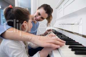 Mother assisting daughter in playing piano