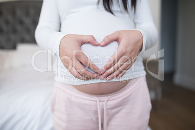 Woman forming heart shape on stomach with hands