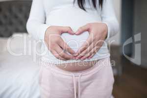 Woman forming heart shape on stomach with hands