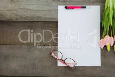 Blank paper with spectacles and tulip kept on wooden table