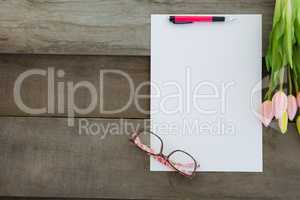 Blank paper with spectacles and tulip kept on wooden table