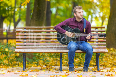 Young man sitting on bench and playing acoustic guitar