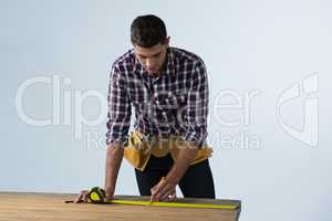 Male architect measuring wooden plank with tape measure