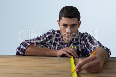 Male architect measuring wooden plank with tape measure