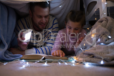 Father and daughter reading book under shelter