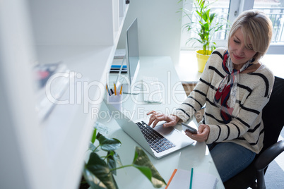 Woman using mobile phone and laptop at table