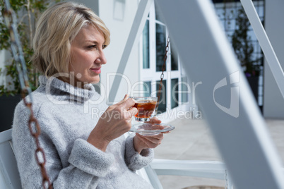 Thoughtful woman having lemon tea in porch