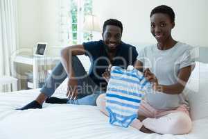 Happy couple holding baby clothes in bedroom