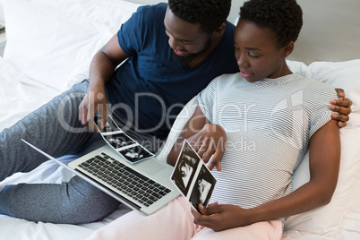 Man and pregnant woman looking at sonography in bedroom