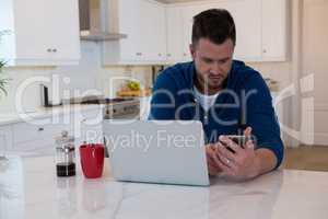 Handsome man using mobile phone in kitchen