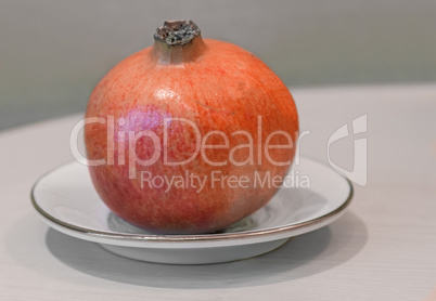 Ripe pomegranate on a white saucer.