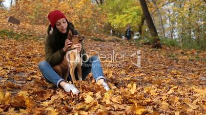 Beautiful girl stroking cute dog in autumn park