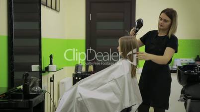 Hairstylist drying girl's hair with blow dryer