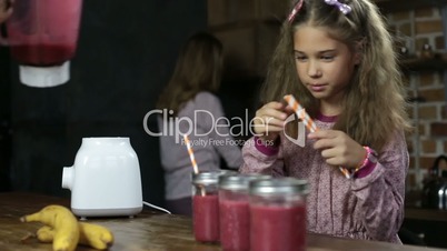 Girl puts drinking straws into jars with smoothie