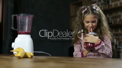 Joyful little girl drinking tasty berry smoothie