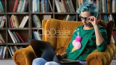 Charming hipster girl typing on laptop in library