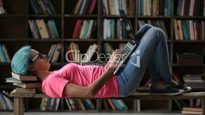 Cute girl with laptop lying on bench in library