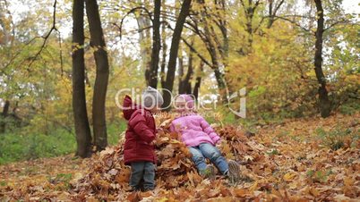 Smiling children jumping in pile of autumn leaves