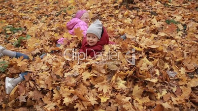 Playful kids lying in pile of yellow foliage