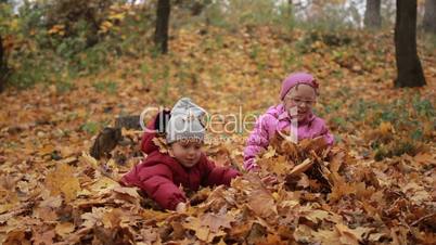 Two happy kids throwing fallen leaves up in fall