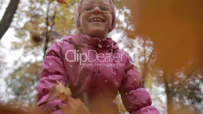 Smiling girl throwing maple leaves in autumn
