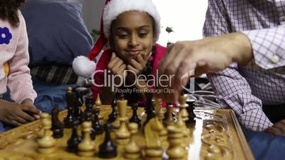 Smiling girl in santa hat watching chess game