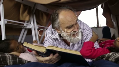 Bearded aged man and grandchildren reading a book