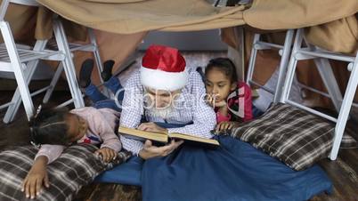 Grandpa in santa hat reading a book with kids