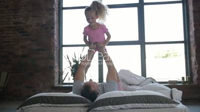 Playful father lifting his daughter on bed at home