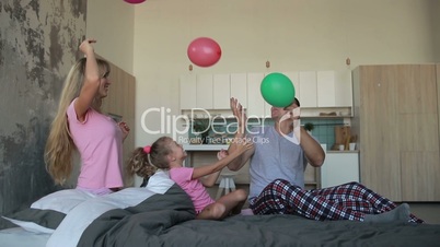 Joyful family playing with balloons on bed