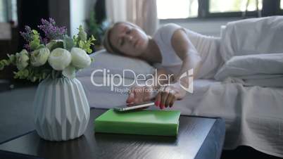 Sleepy woman turning off mobile alarm clock