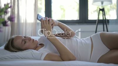 Woman in bed checking social apps with smartphone