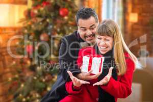 Mixed Race Couple Sharing Christmas In Front of Decorated Tree.