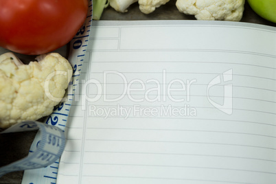 Open diary with vegetables on wooden background