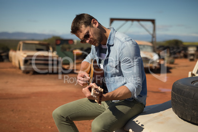 Man playing guitar while sitting on a car