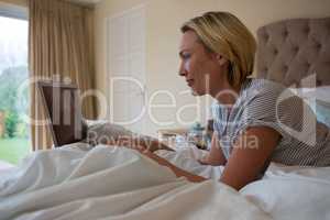 Woman using laptop while relaxing on bed