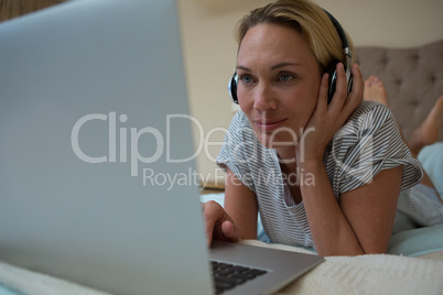 Woman using laptop while listening music on headphones