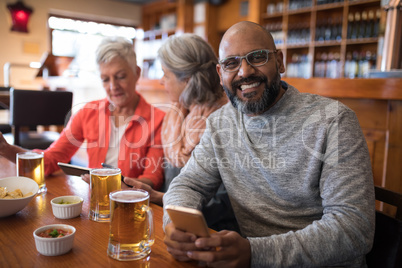 Senior friends using mobile phone in bar