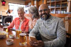 Senior friends using mobile phone in bar