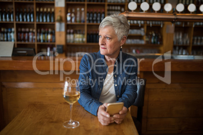 Senior woman with mobile phone sitting in restaurant