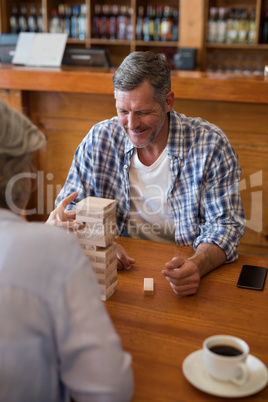 Senior friends playing jenga game on table in bar