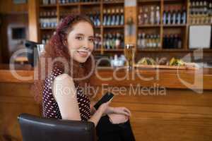 Beautiful woman sitting on chair and using mobile phone at counter