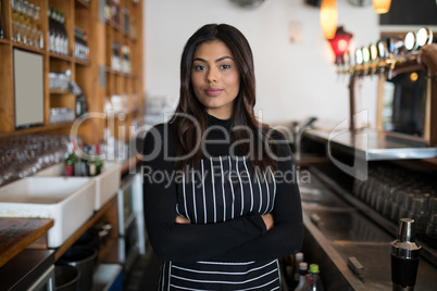 Beautiful waitress standing with arms crossed in bar