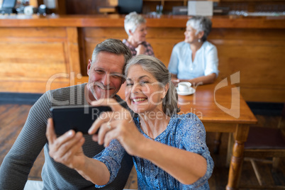 Senior couple taking selfie with mobile phone in restaurant